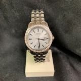 Silver wristwatch on a white display stand against a dark background.