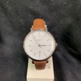 Brown leather wristwatch with a white face displayed on a stand