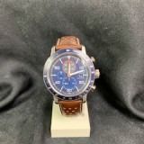 Blue wristwatch with brown leather strap on a stand against a dark fabric background