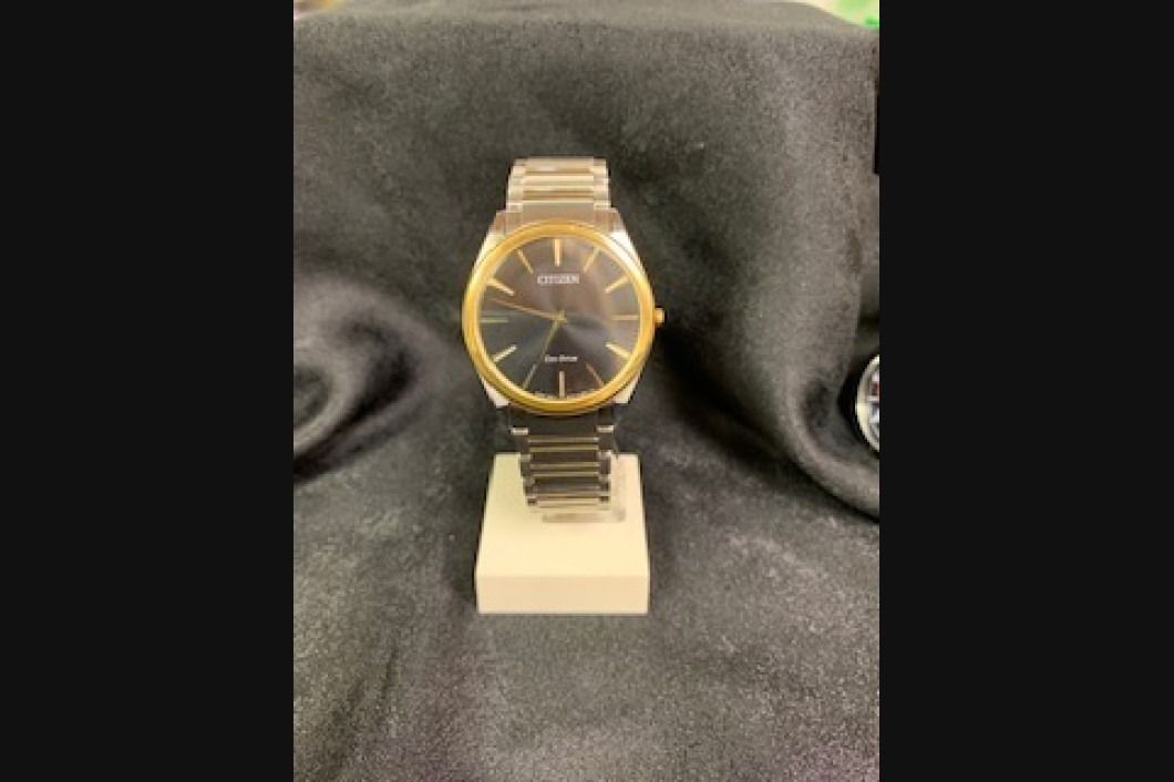 Gold-tone watch with a black face displayed on a small stand against a dark fabric background