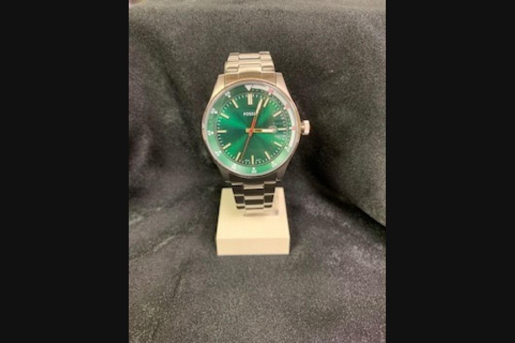 Silver wristwatch with a green face displayed on a stand against a dark fabric background