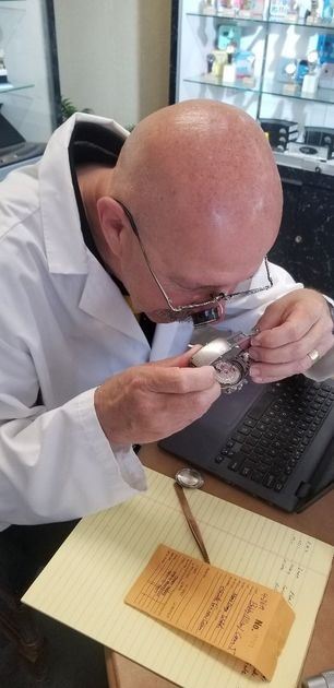 Man examining a small object with a magnifying glass at a desk with a keyboard and notebook