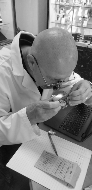 Person in a lab coat inspecting a sample with a magnifier next to a laptop and notebook.