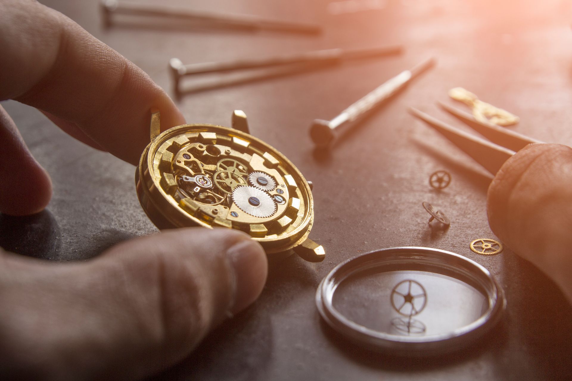 Hands assembling a gold watch movement with tools on a workbench
