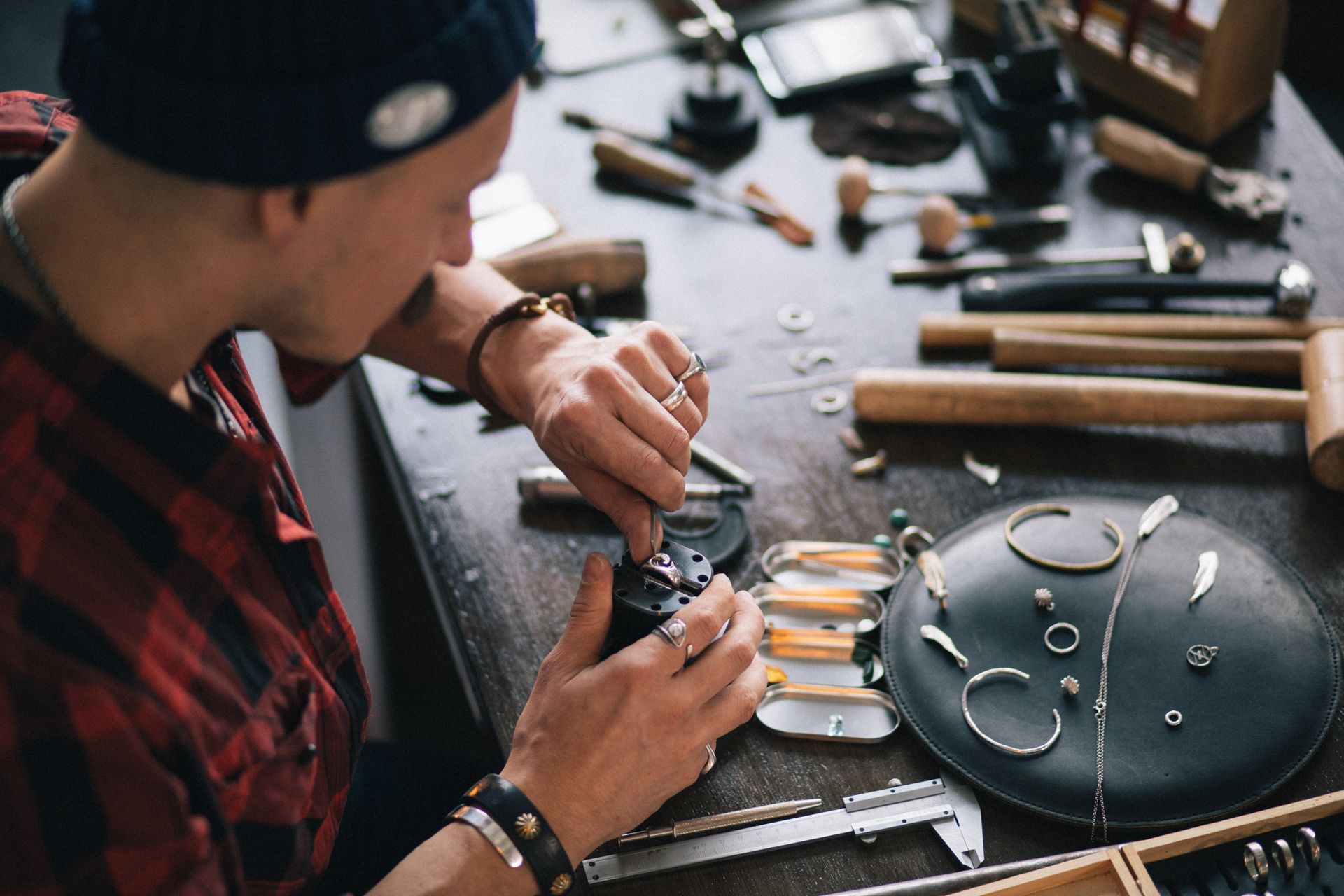 Person assembling a wristwatch at a workbench with tools and watch parts spread out.