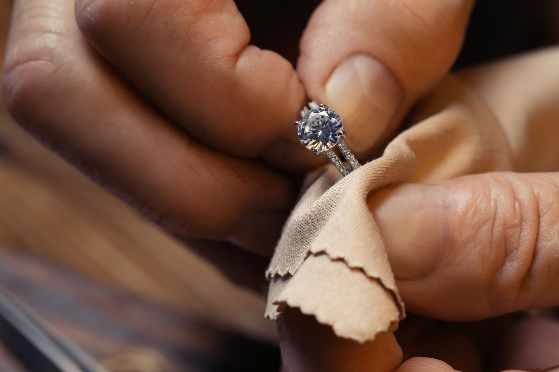 Hands polishing a diamond ring with a beige cloth.