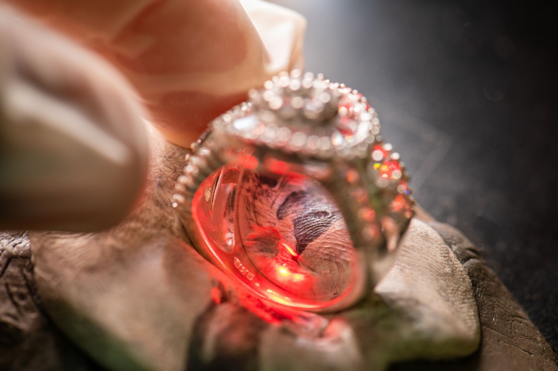 Close-up of a hand holding a diamond ring glowing red under light on a dark surface