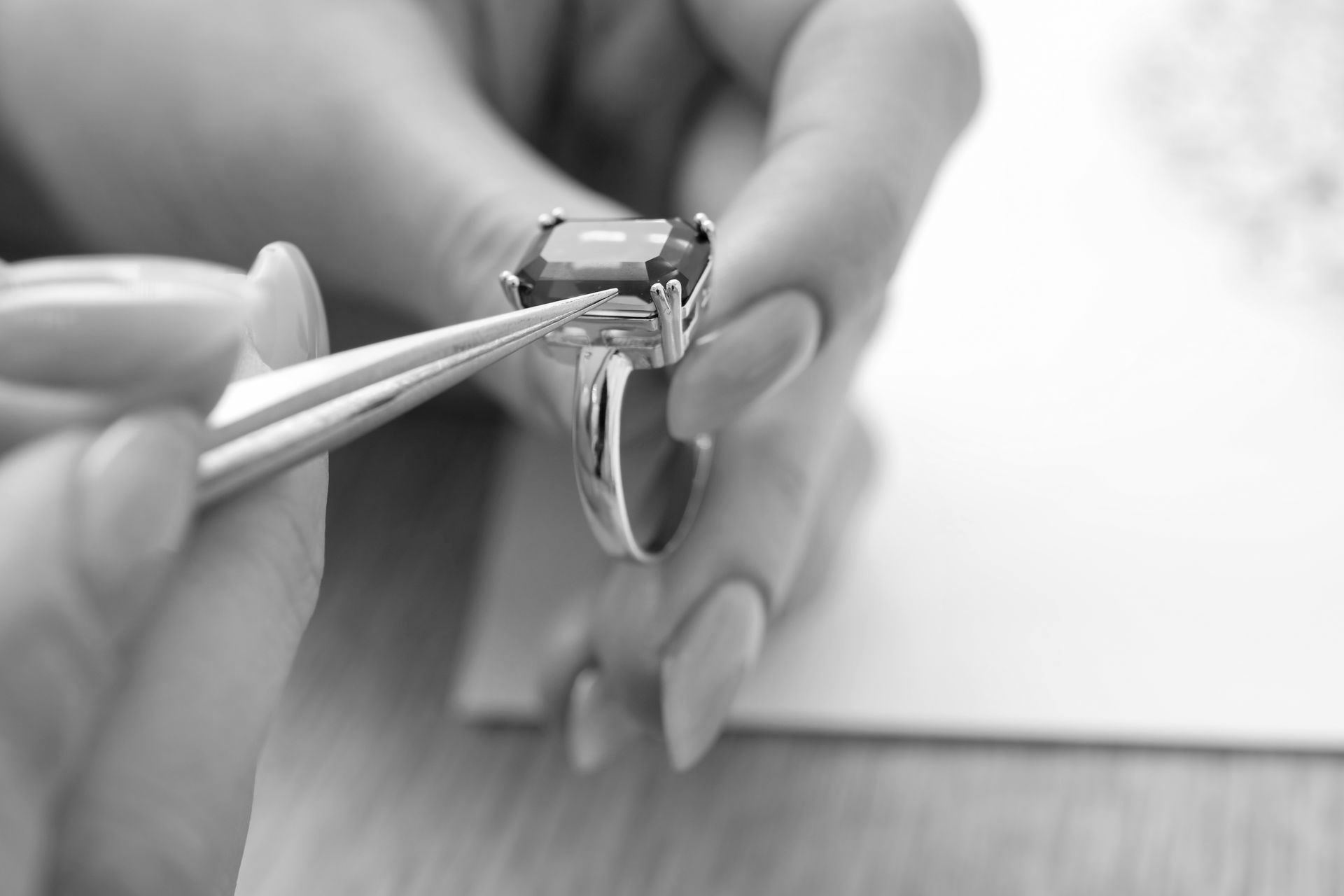 Hands using tweezers to adjust a diamond ring on a white surface