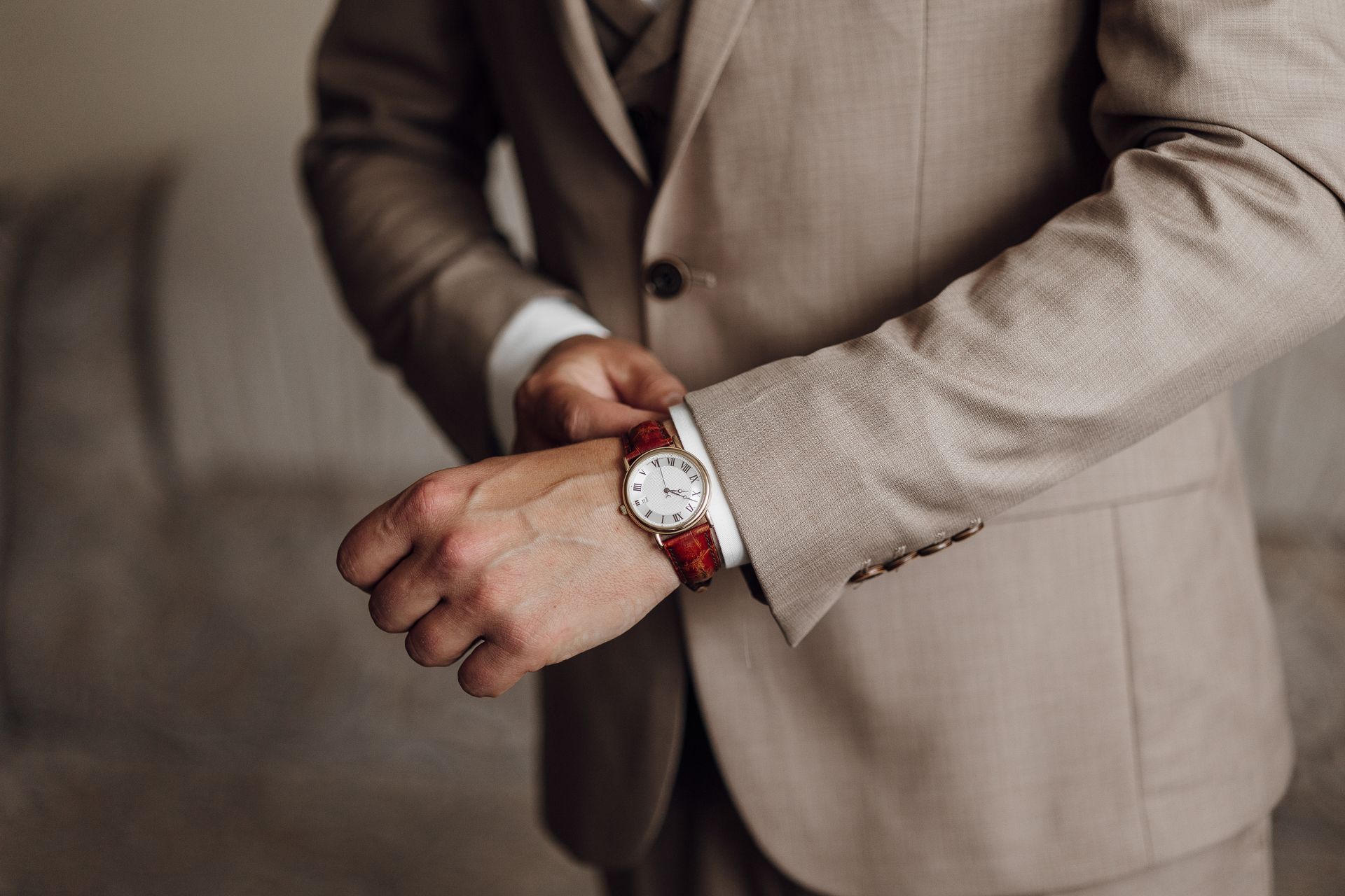 Person adjusting a beige suit jacket with a red wristwatch on the left wrist
