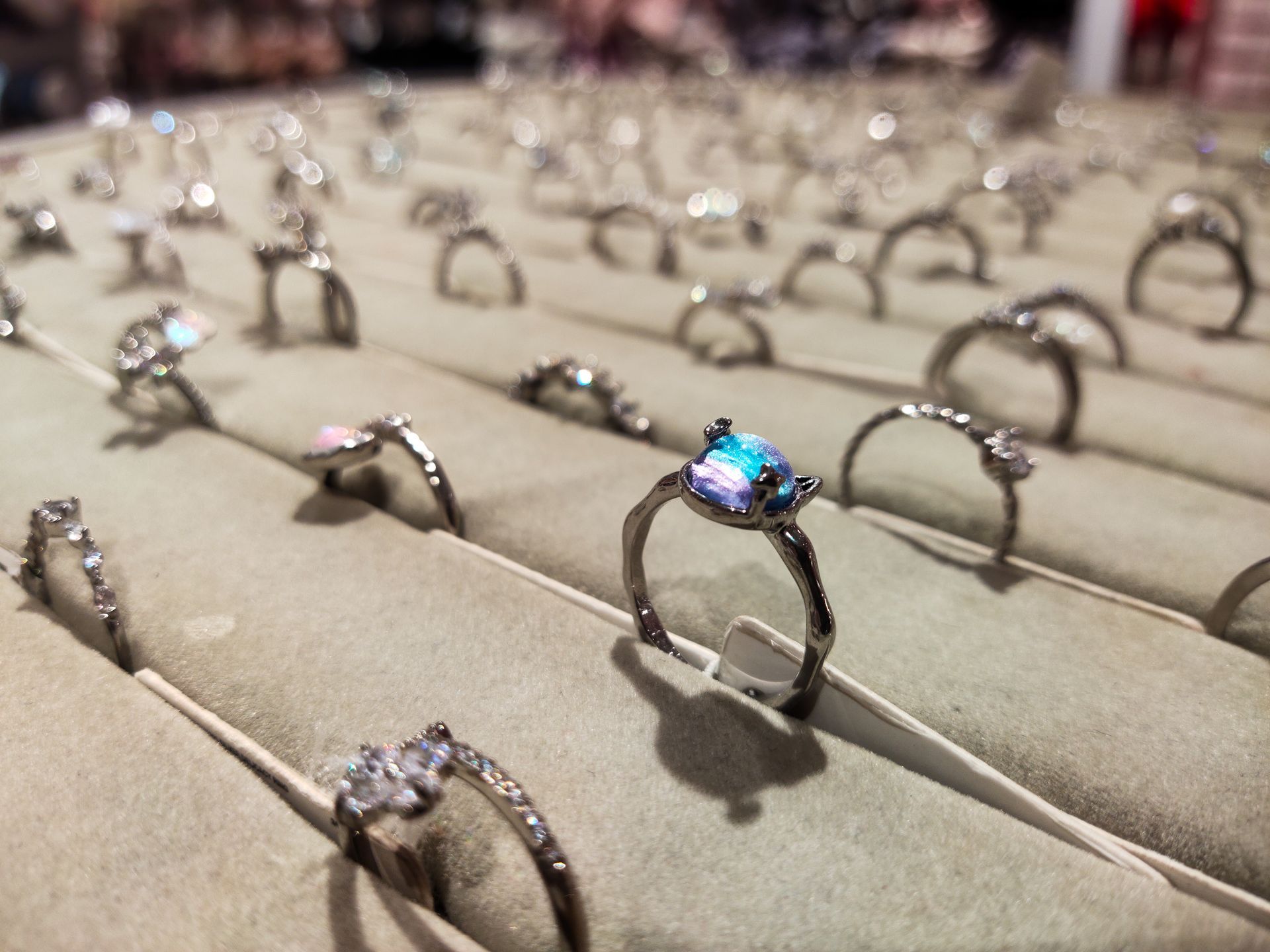 Rows of silver rings with colorful gemstones displayed on beige velvet trays