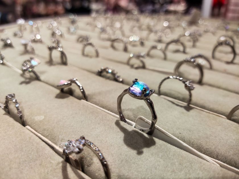 Rows of gemstone rings displayed on beige stands, with one blue stone ring in focus