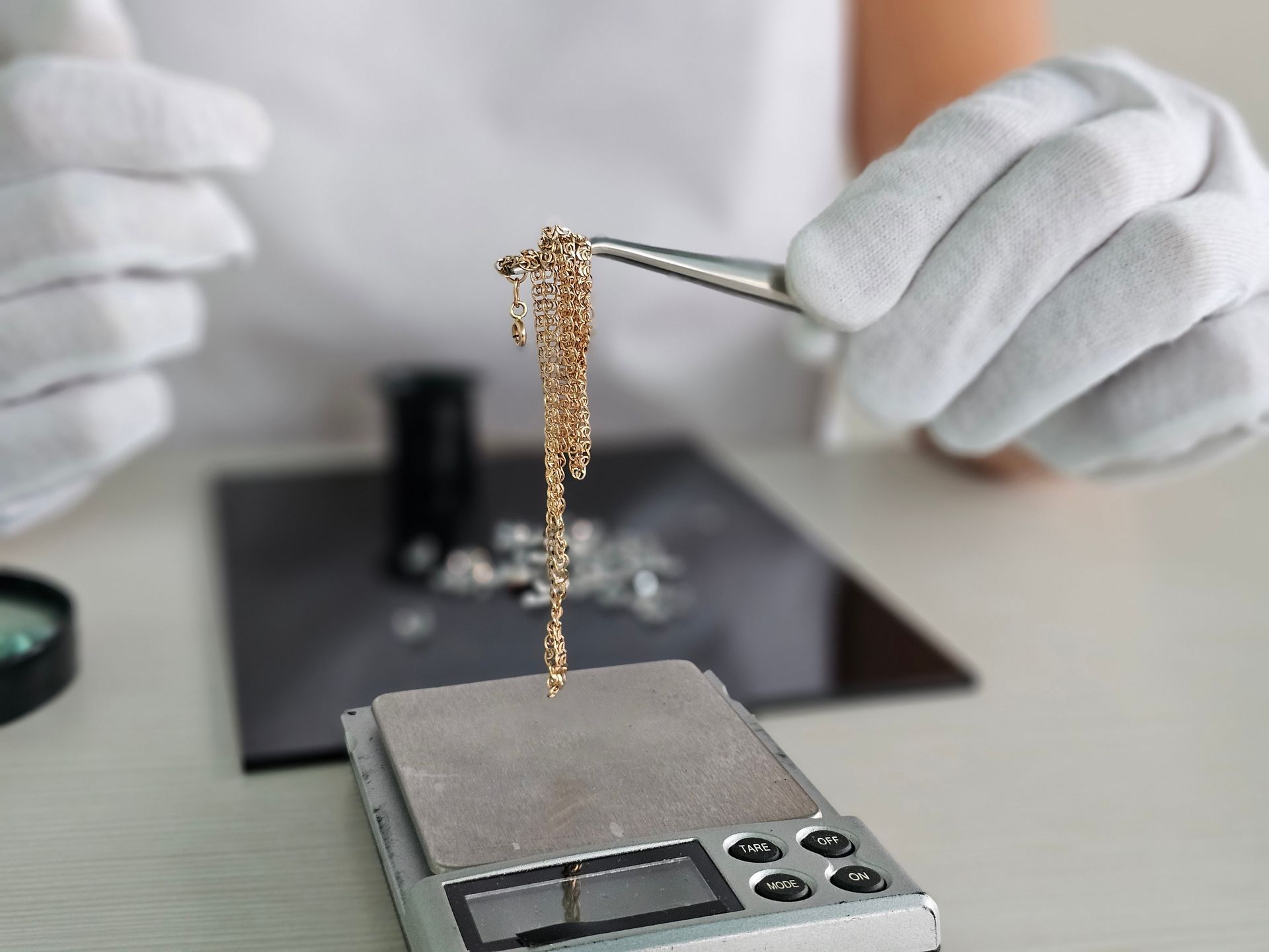 Gloved hands holding a gold necklace above a digital scale in a jewelry appraisal setting