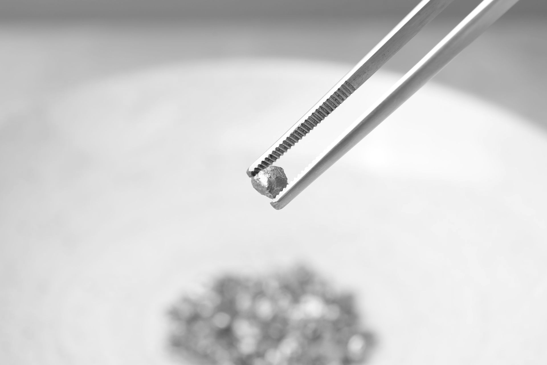 Tweezers holding a small clear gemstone above a blurred pile of gems