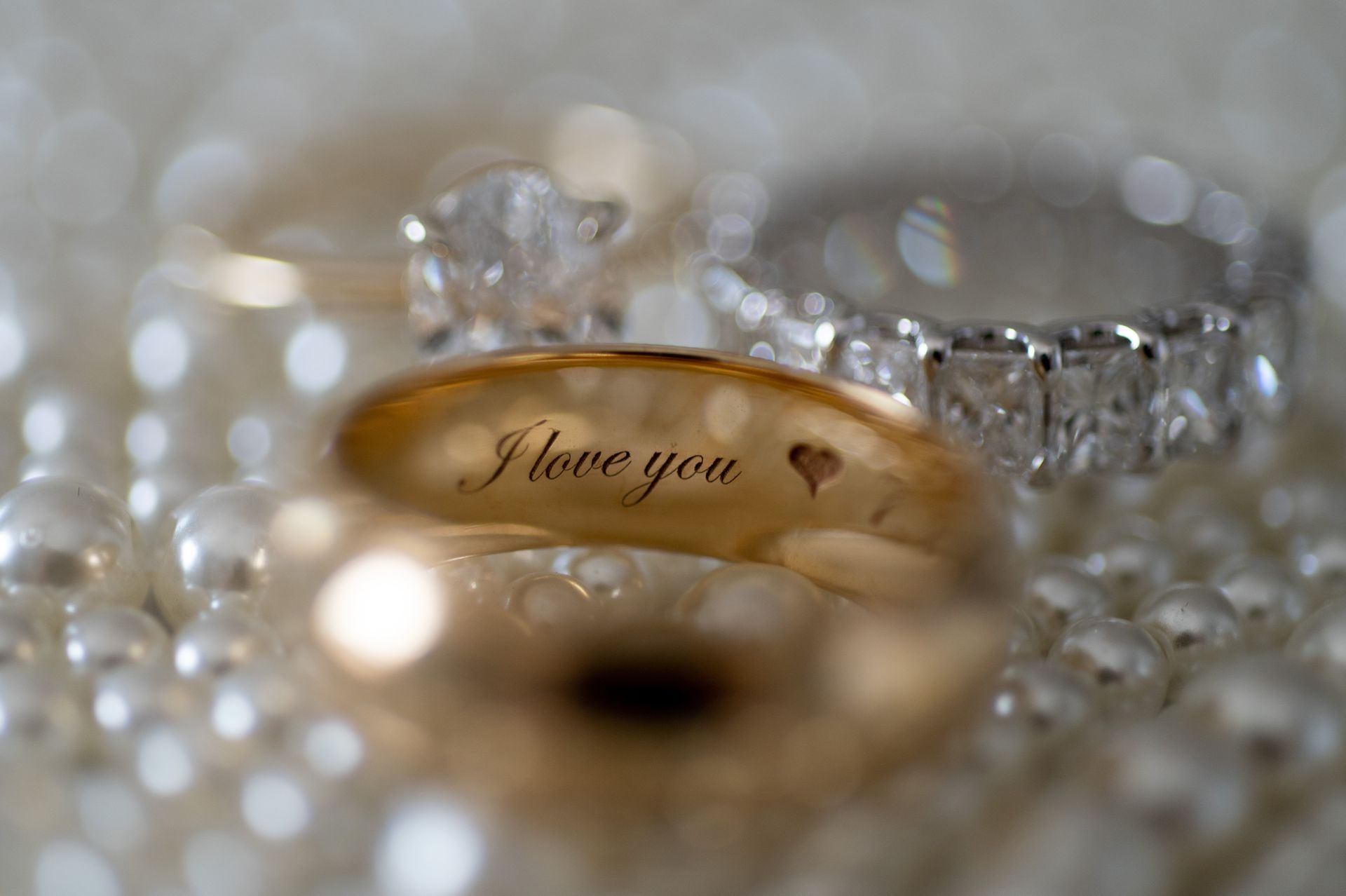 Wedding rings on pearls, including a gold band engraved “I love you” and a diamond ring.