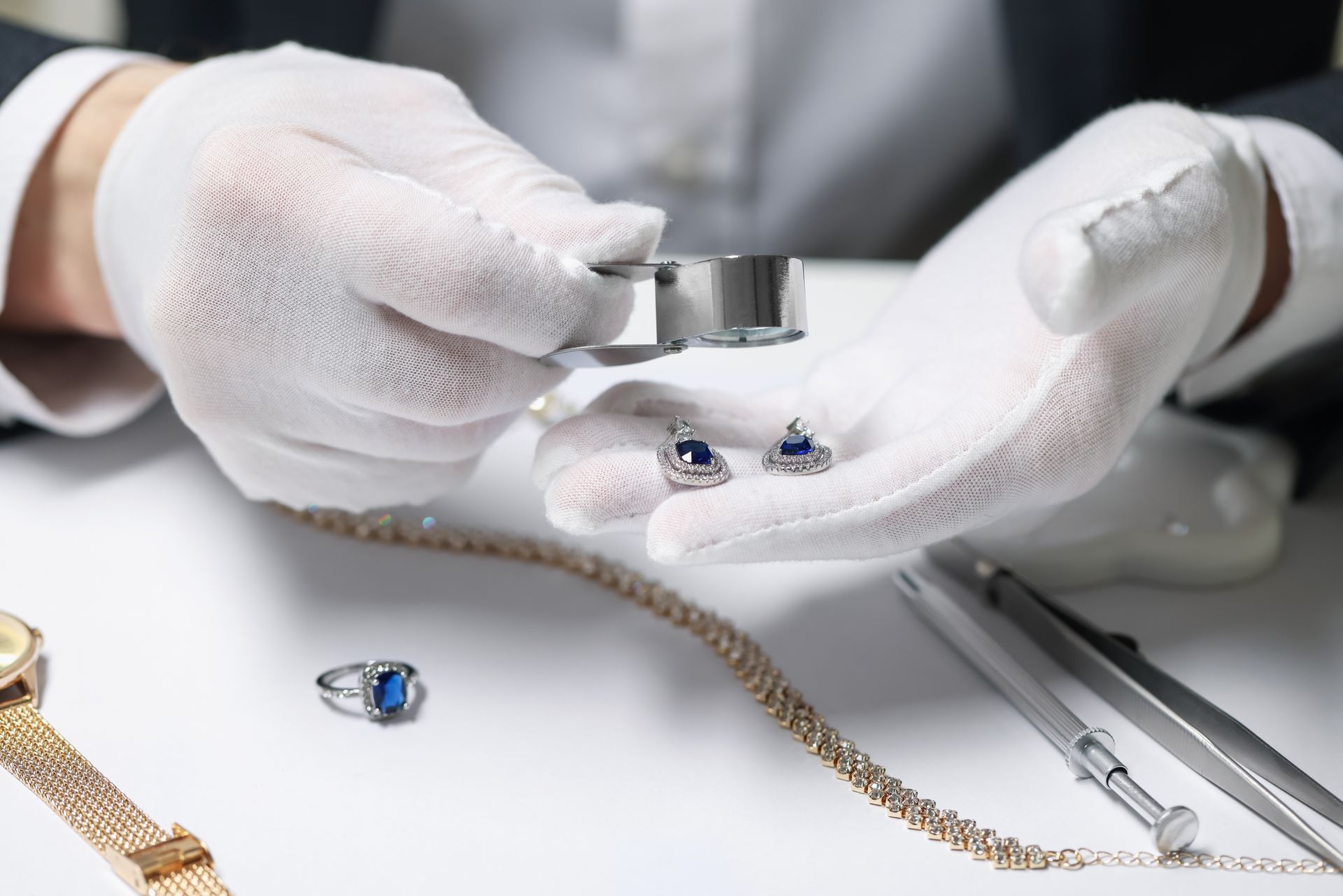 Gloved hands examining blue gemstones with a jeweler’s loupe on a worktable