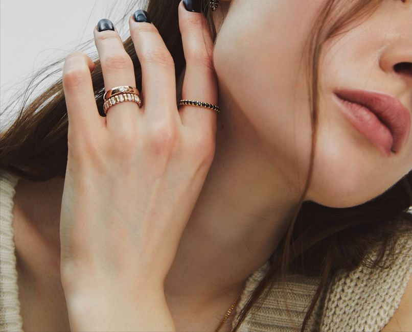 Close-up of a hand with stacked rings resting near a woman's face and neck