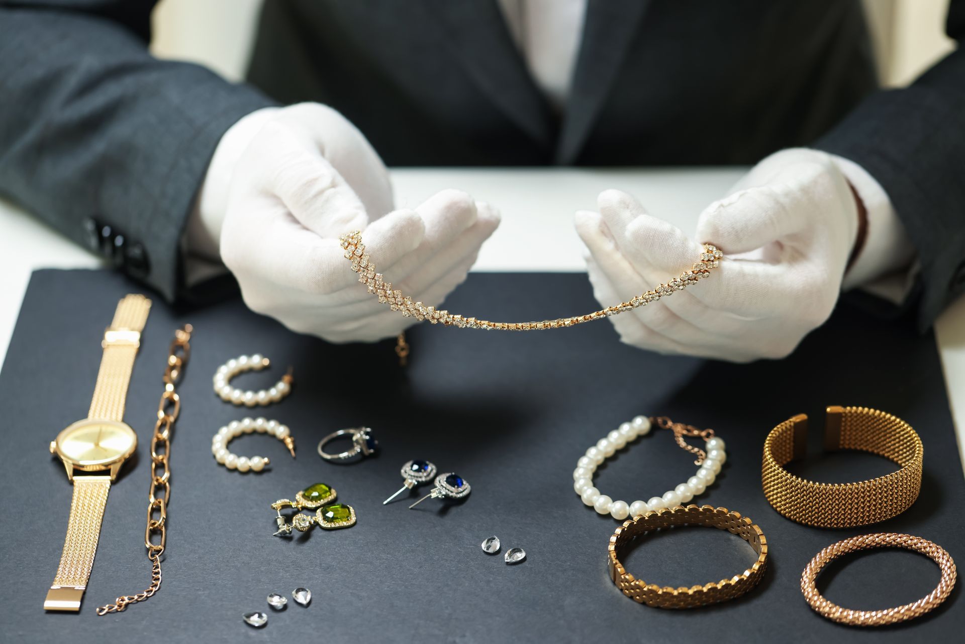 Gloved hands examining gold jewelry pieces laid out on a dark table