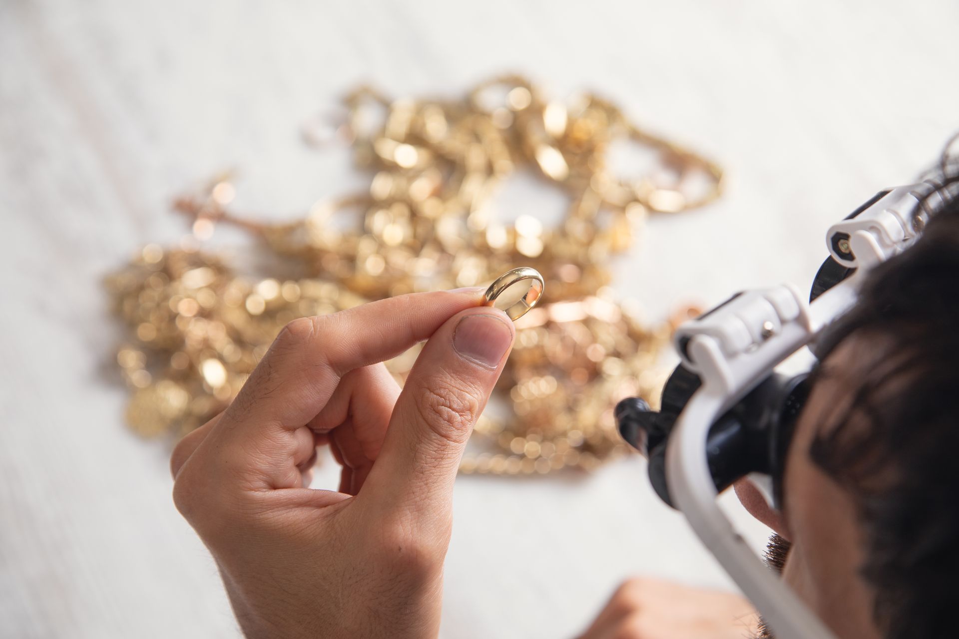 Hand holding a gold ring with jewelry and a magnifying loupe on a white table
