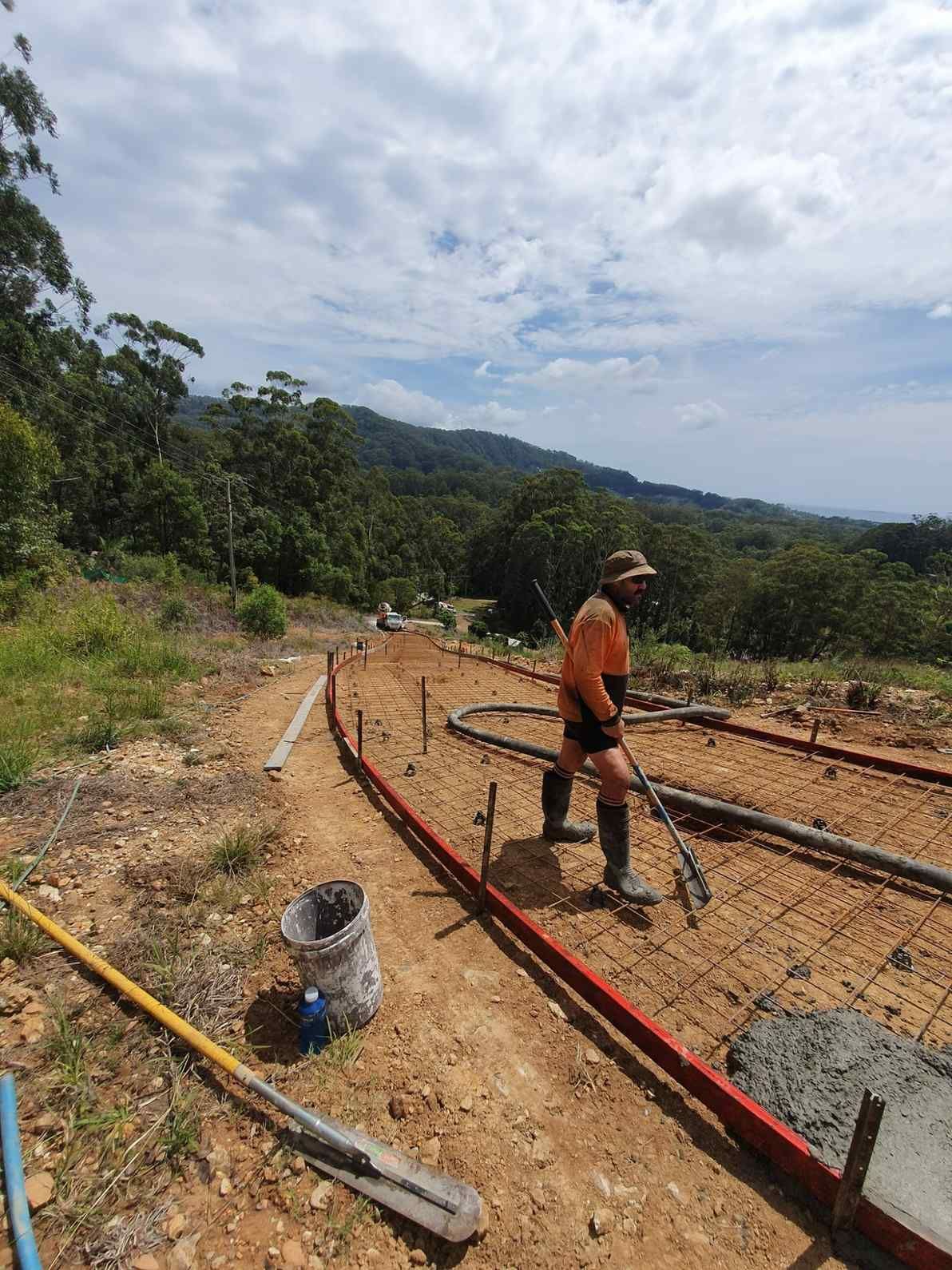 A Man is Standing on a Dirt Road Holding a Hose — Felto's Concrete Line Pumping in Sawtell, NSW