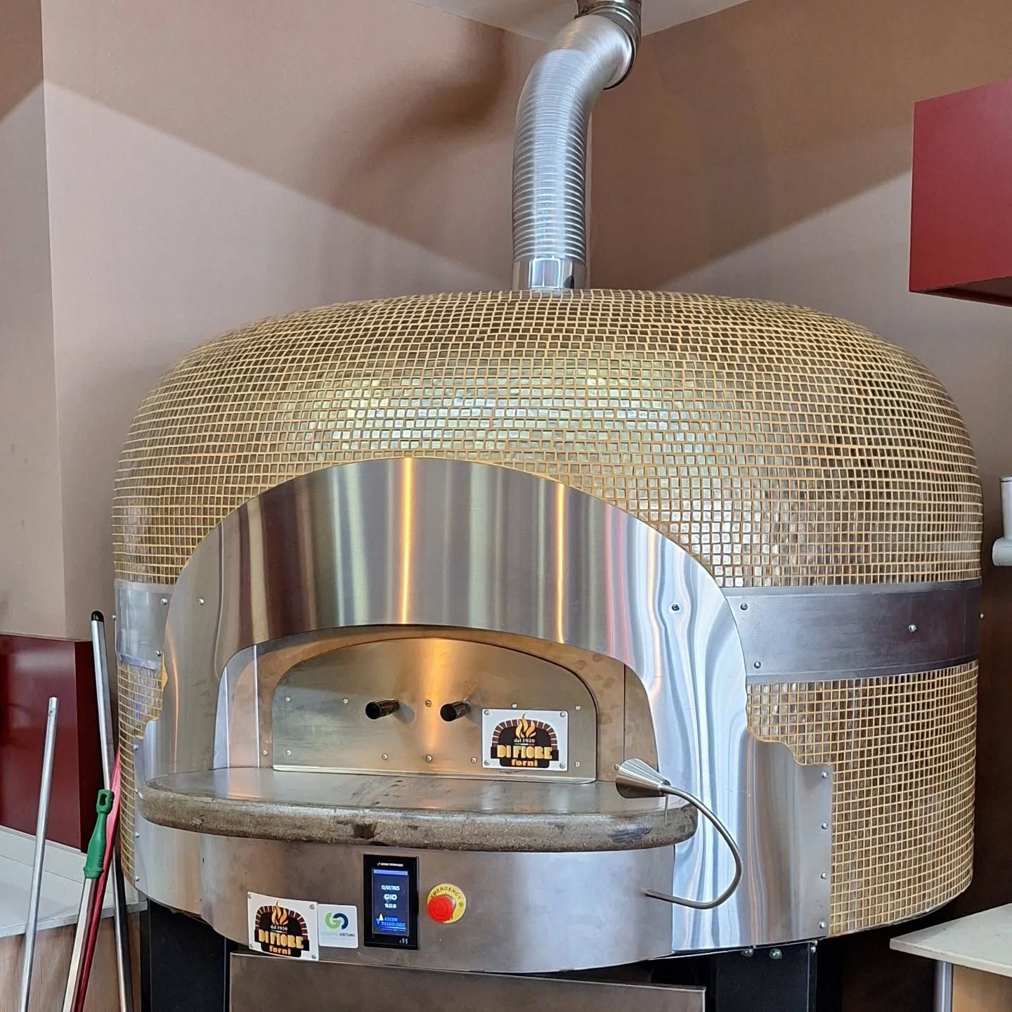 Forno per pizza professionale rivestito in vimini con frontale e camino in acciaio inox, installato nella cucina di un ristorante.