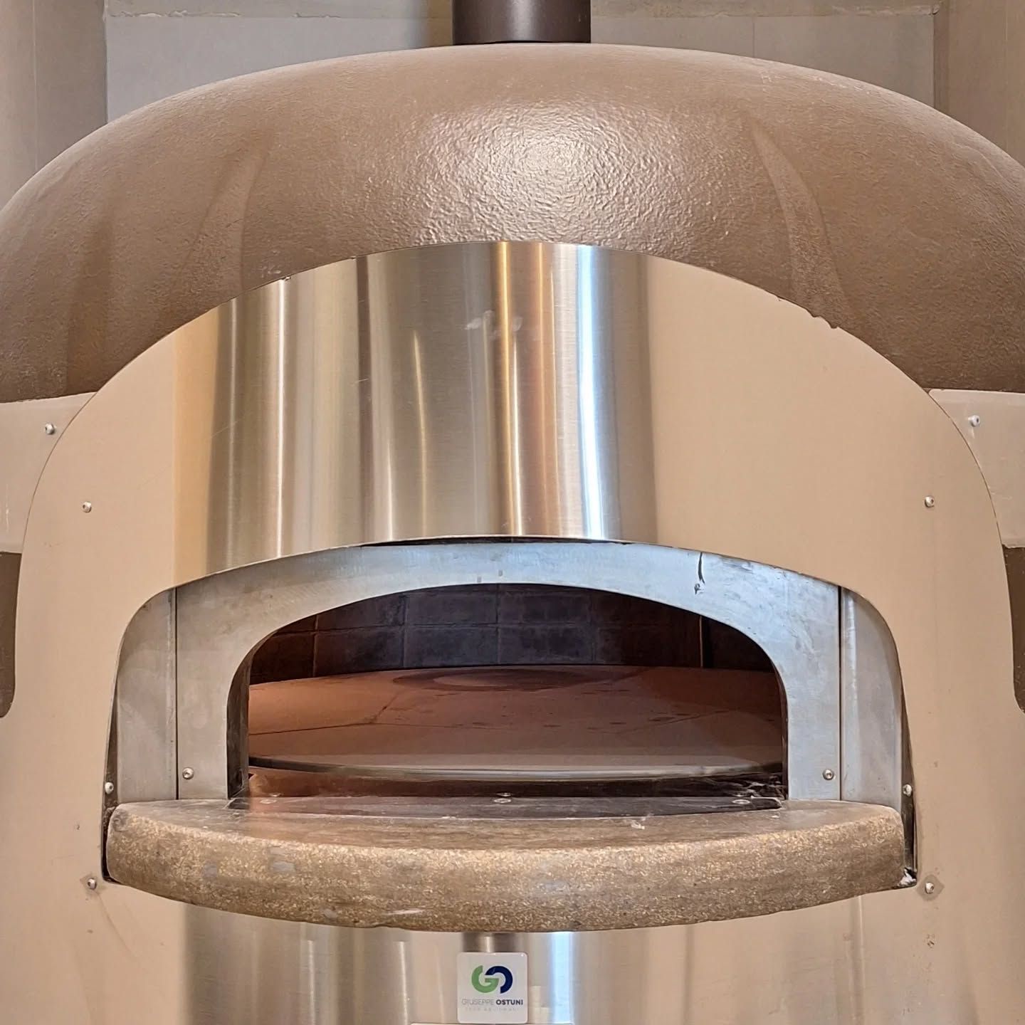 Forno per pizza da banco in acciaio inox e beige, con frontale aperto e superficie di cottura in pietra.