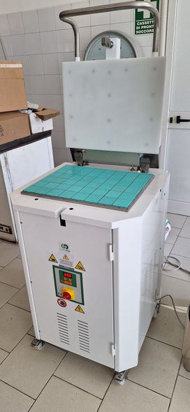 Macchinario industriale bianco con etichette di sicurezza, posizionato in un'officina o in un ambiente di fabbrica.