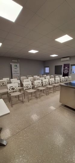 Mensa vuota con file di sedie e tavoli sotto luci fluorescenti a soffitto; distributori automatici sulla destra.