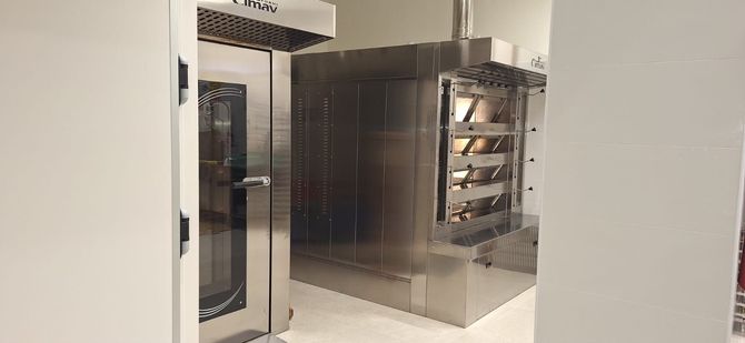Impastatrice professionale e tramoggia per farina in un panificio vicino a finestre luminose