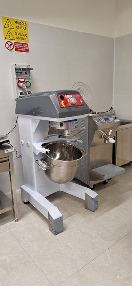 Macchina per panificazione in acciaio inox all'interno di una cucina commerciale pulita, con vassoi trasportatori e pannelli di controllo.