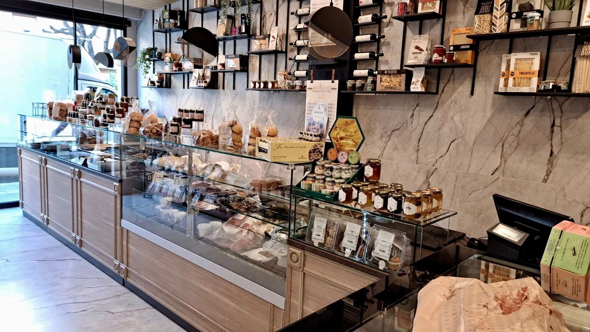 Vetrina in vetro in un accogliente caffè, piena di pasticcini e dessert, con scaffali pieni di barattoli e decorazioni alle sue spalle.