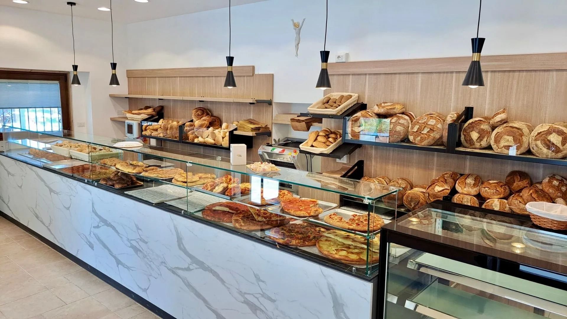 Banco espositivo da panetteria con assortimento di pane e pasticcini sotto luci sospese.