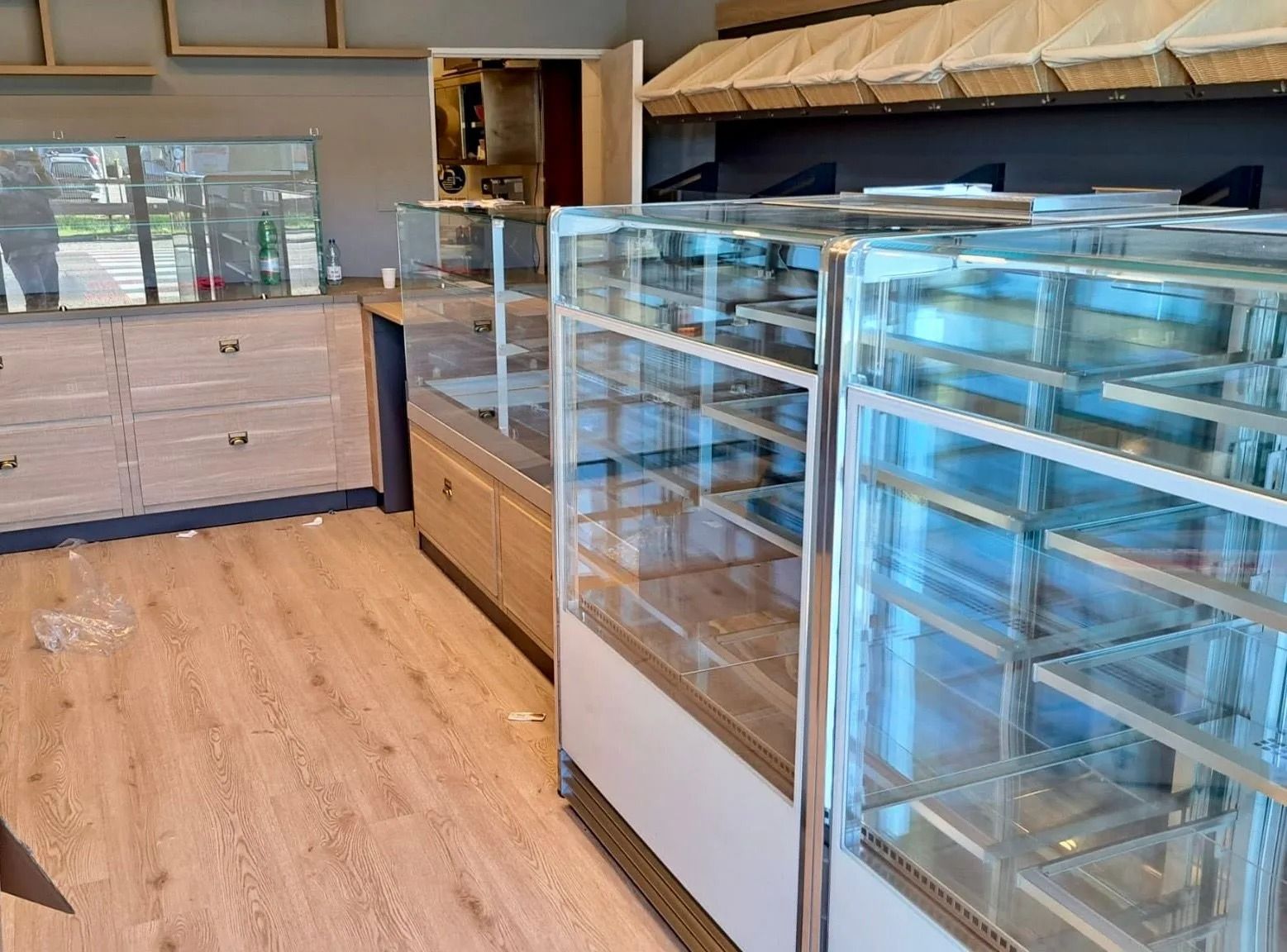Vetrine vuote da forno e banconi in legno in un interno di negozio luminoso e moderno.
