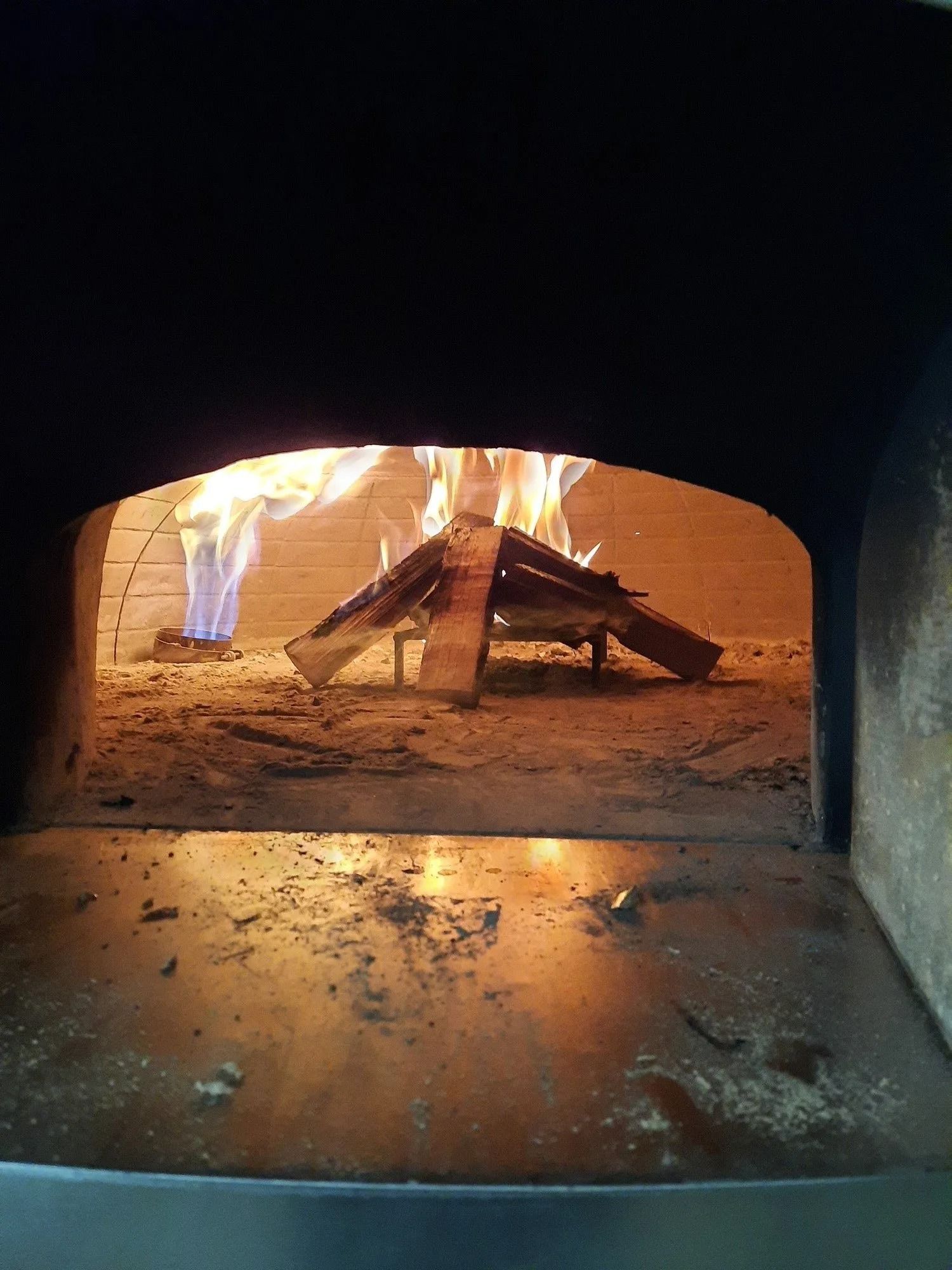 Fiamme all'interno di un forno a legna, con un vassoio di metallo e cenere sul pavimento.