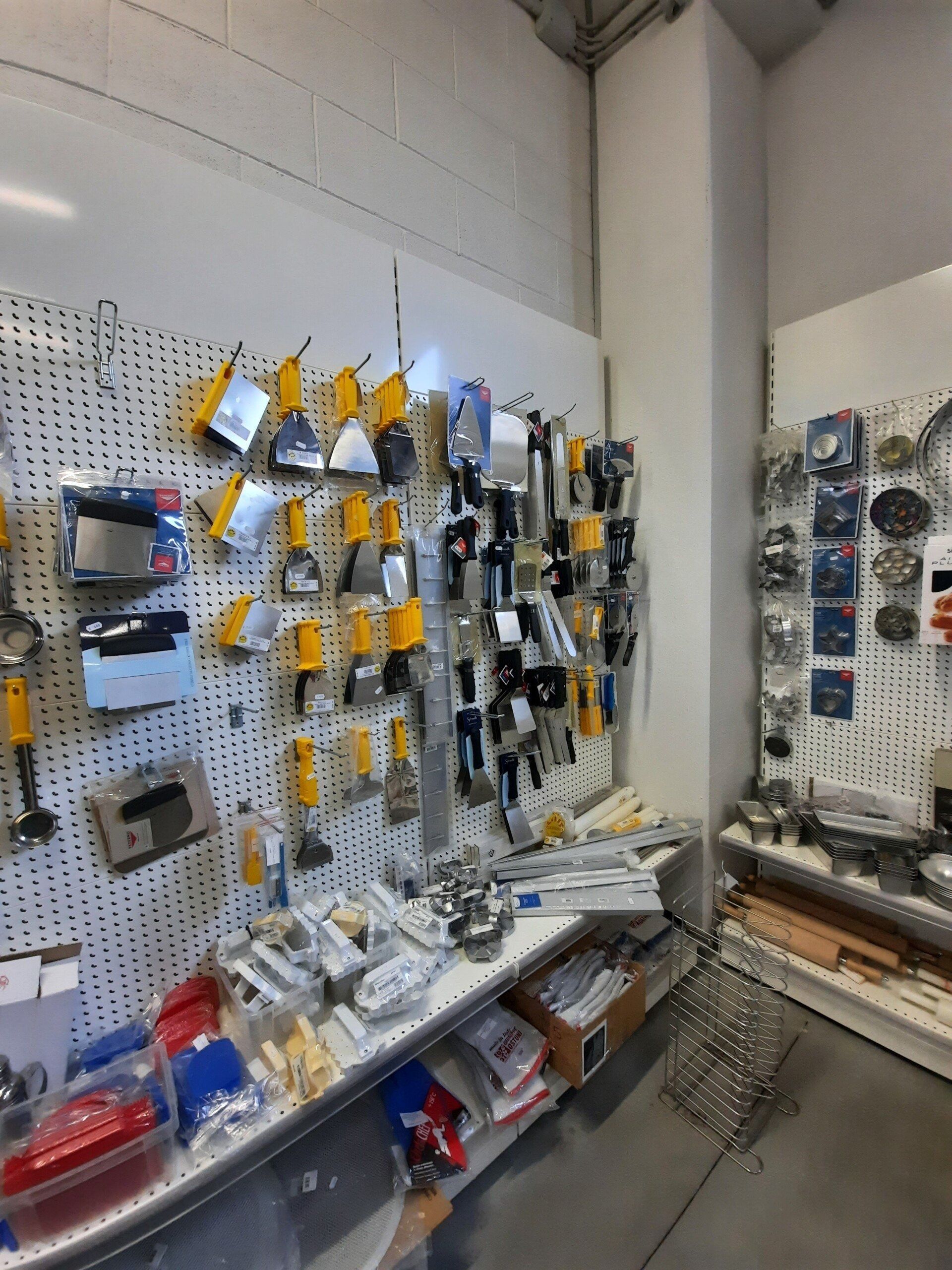 Parete forata con attrezzi e ferramenta assortiti in un corridoio di un'officina, completa di scaffali e contenitori.