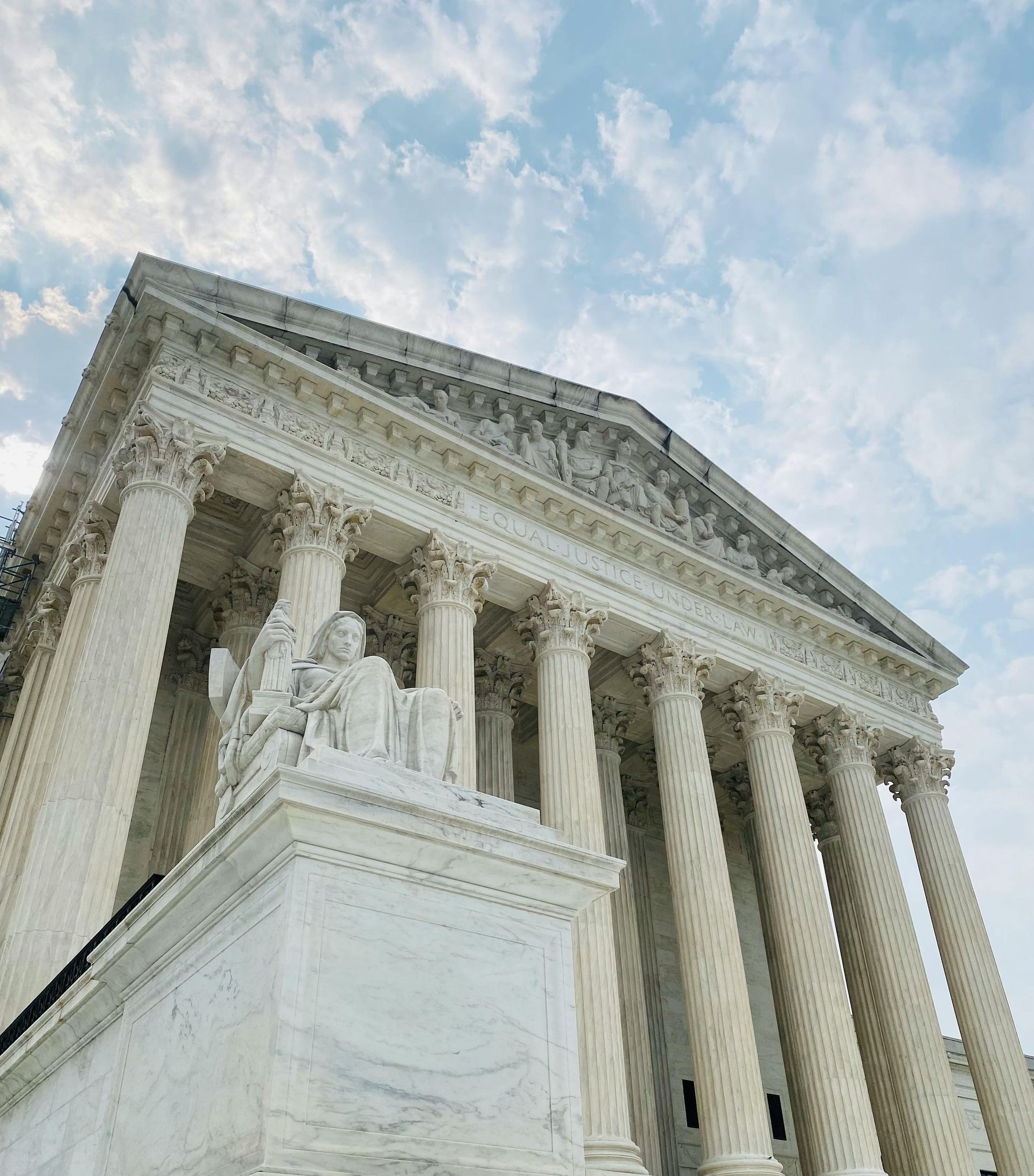 A low-angle view of the white marble Supreme Court building with tall columns under a blue, cloudy sky.