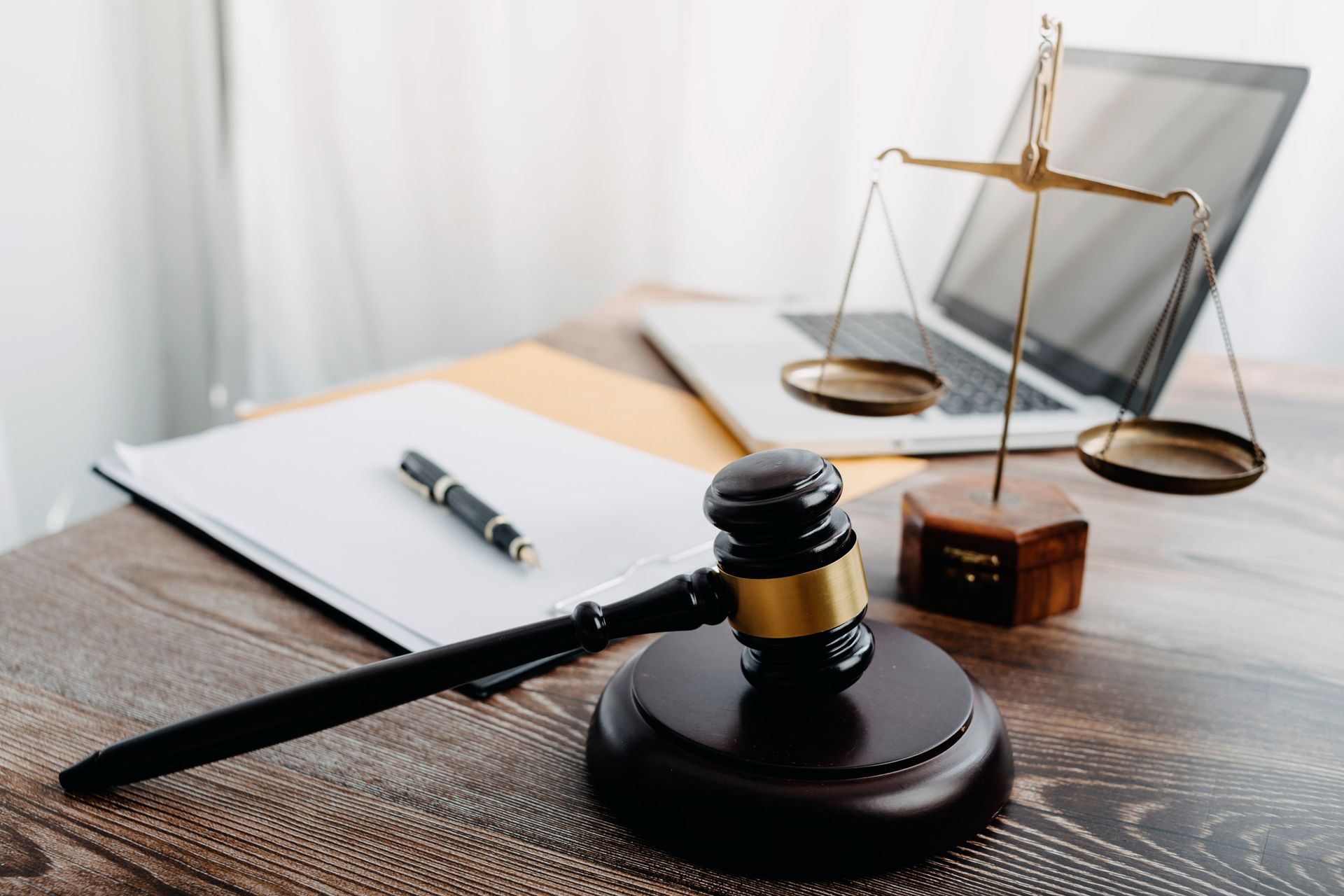 A wooden gavel, a paper document with a pen, and a scale of justice on a desk in front of an open laptop.