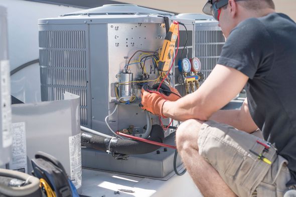 Technician in gloves repairing outdoor HVAC unit with tools and exposed wiring
