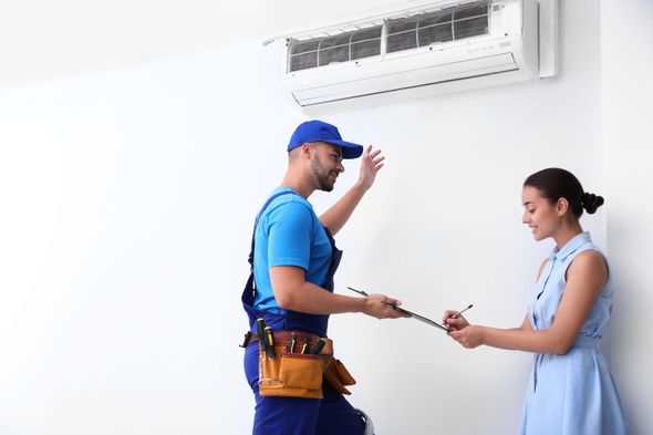 Technician handing a tool to a smiling customer beneath a wall-mounted air conditioner
