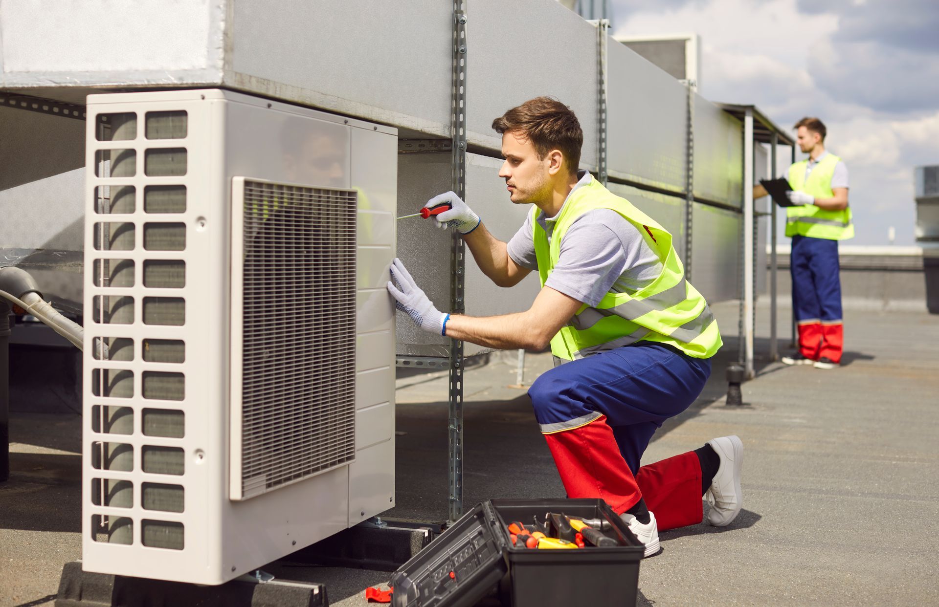Two HVAC technicians are installing a ventilation system on a commercial roof.