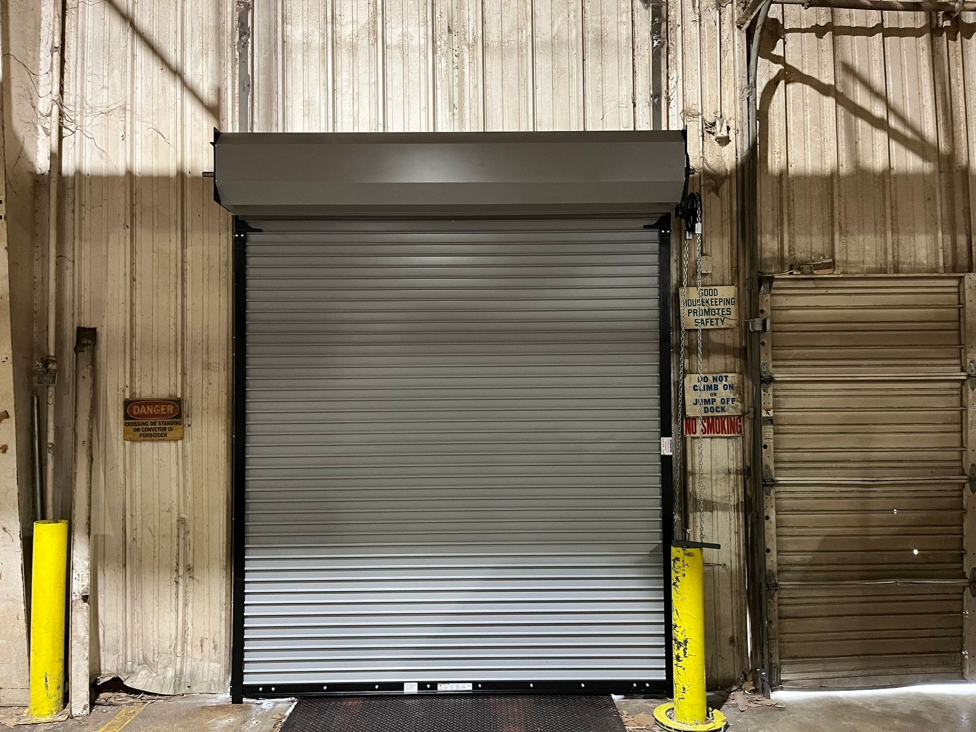 Closed metal roll-up door in a warehouse with yellow bollards and corrugated walls