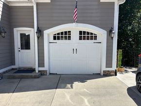 Gray house garage with white door and side entrance under an American flag.