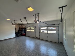 Empty two-car garage with speckled floor, white walls, ceiling storage racks, and closed garage doors.
