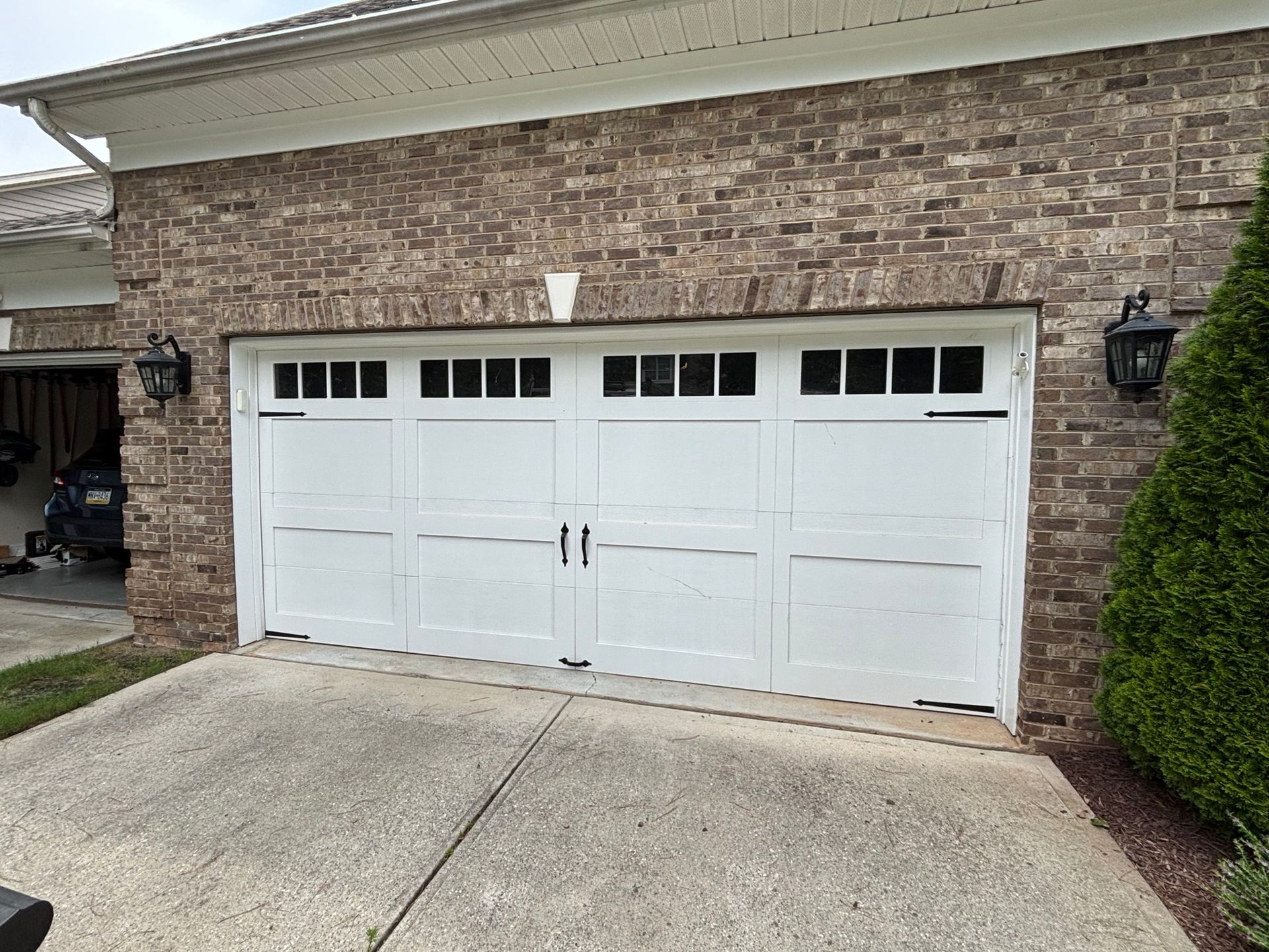 White double garage door on a brick house with a concrete driveway and trimmed shrubbery