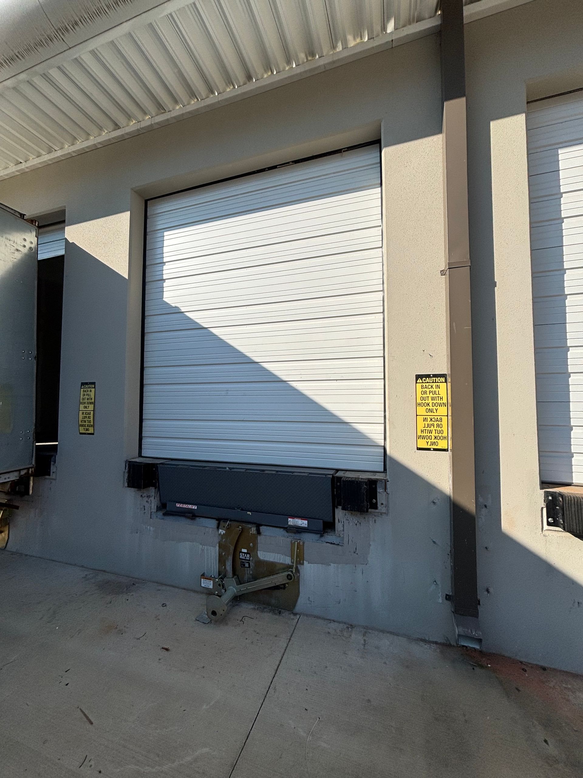 Closed white loading dock door beside a dock leveler on a concrete warehouse wall