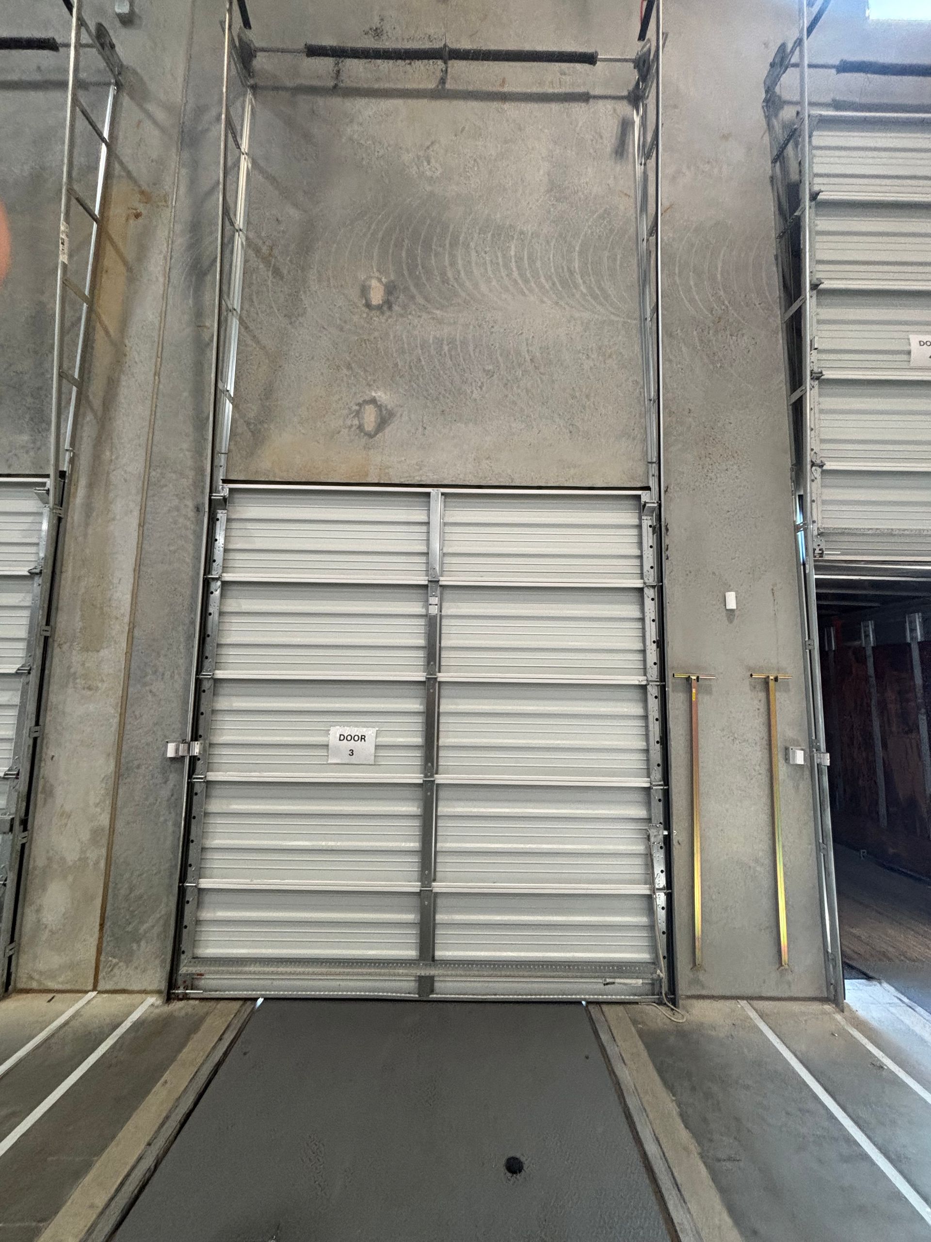 Industrial loading dock with closed metal bay door and concrete walls at the end of a narrow lane.