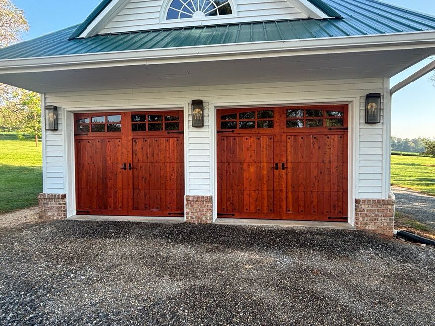 Two wooden garage doors beneath a blue metal roof on a gravel driveway
