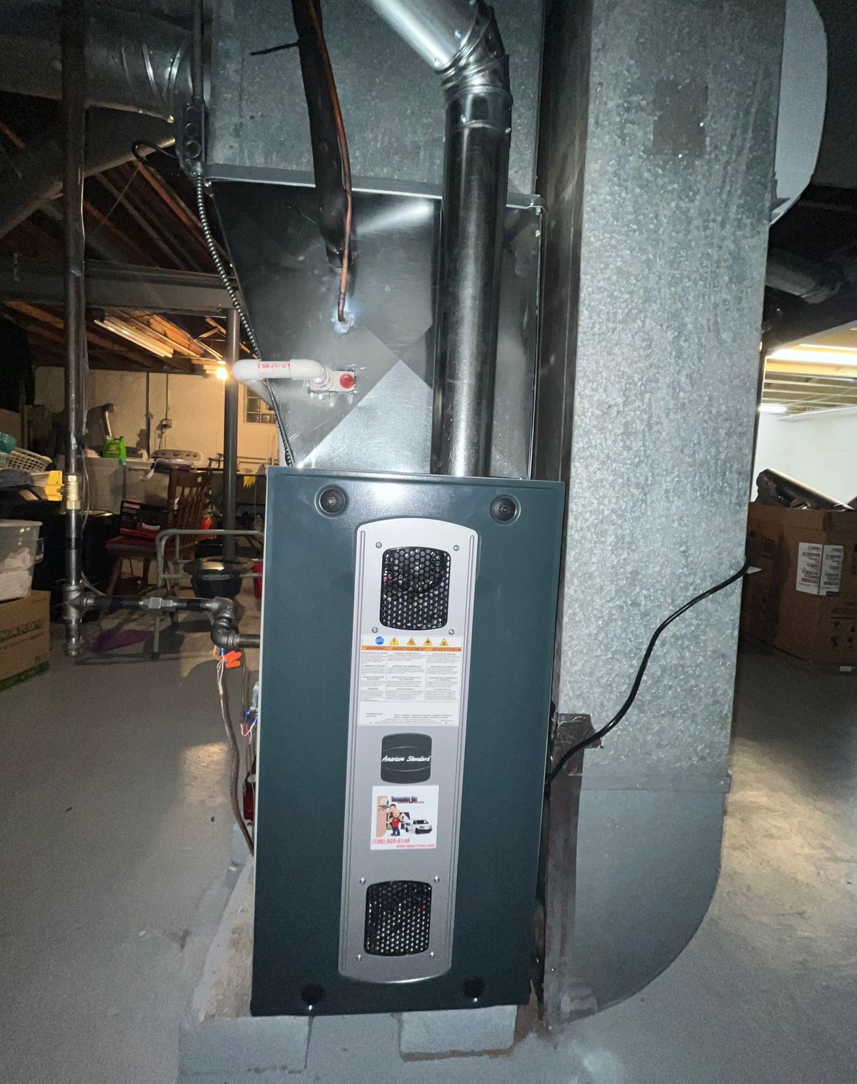 Furnace in a basement, gray metal and ductwork, electrical wires.