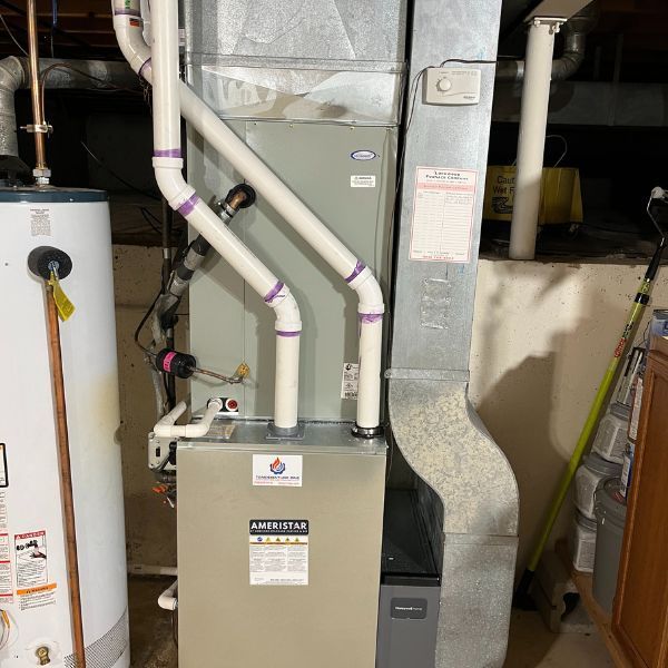 Furnace, water heater, and ductwork in a utility room. Gray and white appliances against a tan wall.