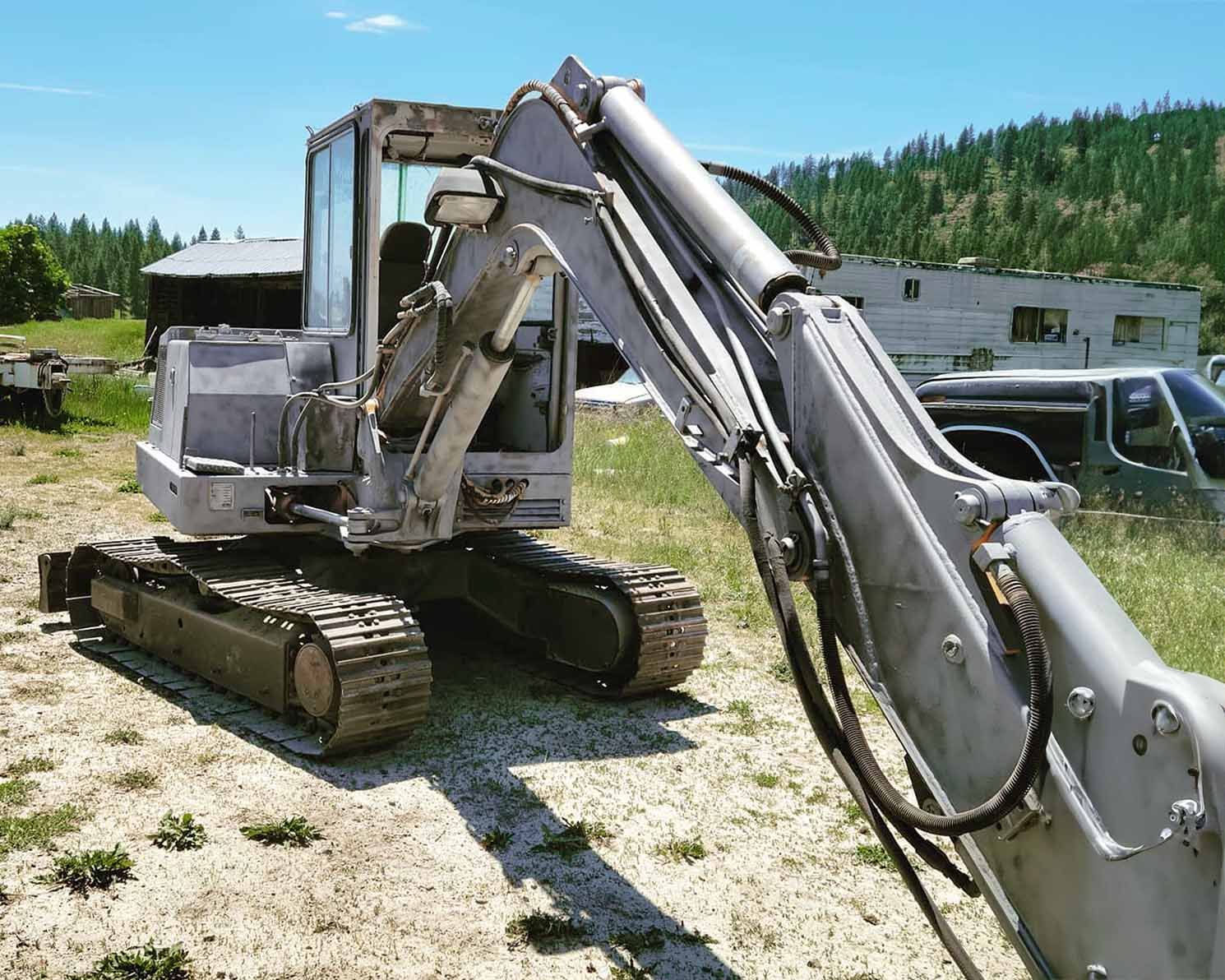 An excavator is parked in a field with a camper in the background