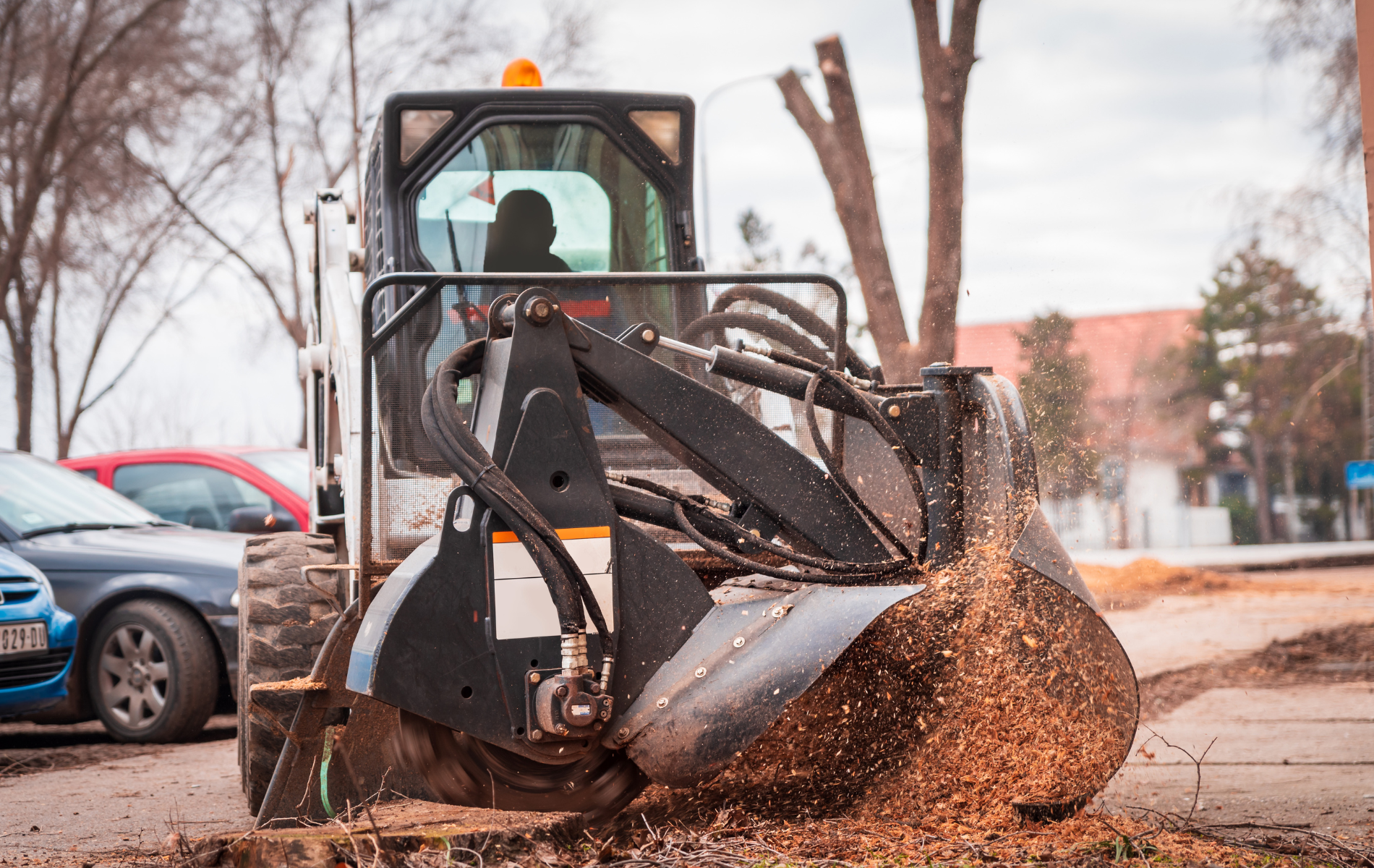 A bulldozer is cutting a tree stump in a parking lot.